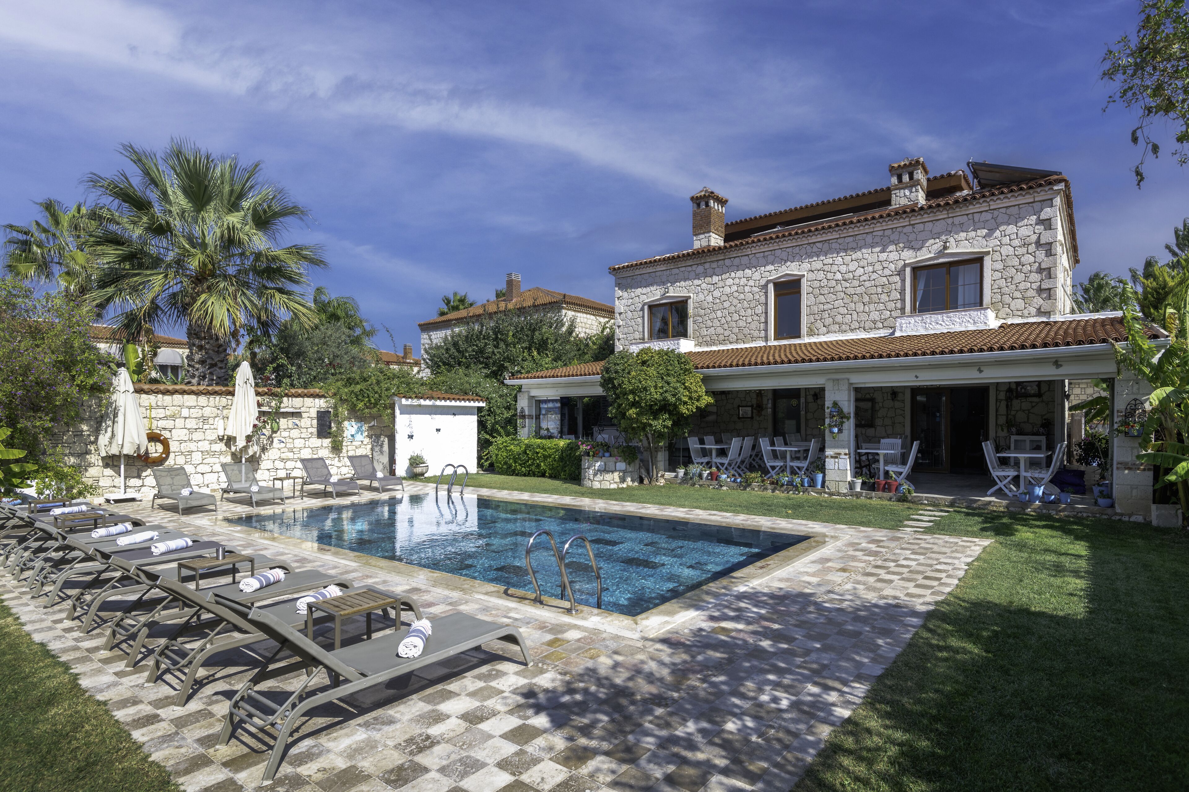 A poolside area with lounge chairs, a stone building, and a clear blue sky.