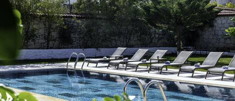 A swimming pool with lounge chairs and a stone wall.