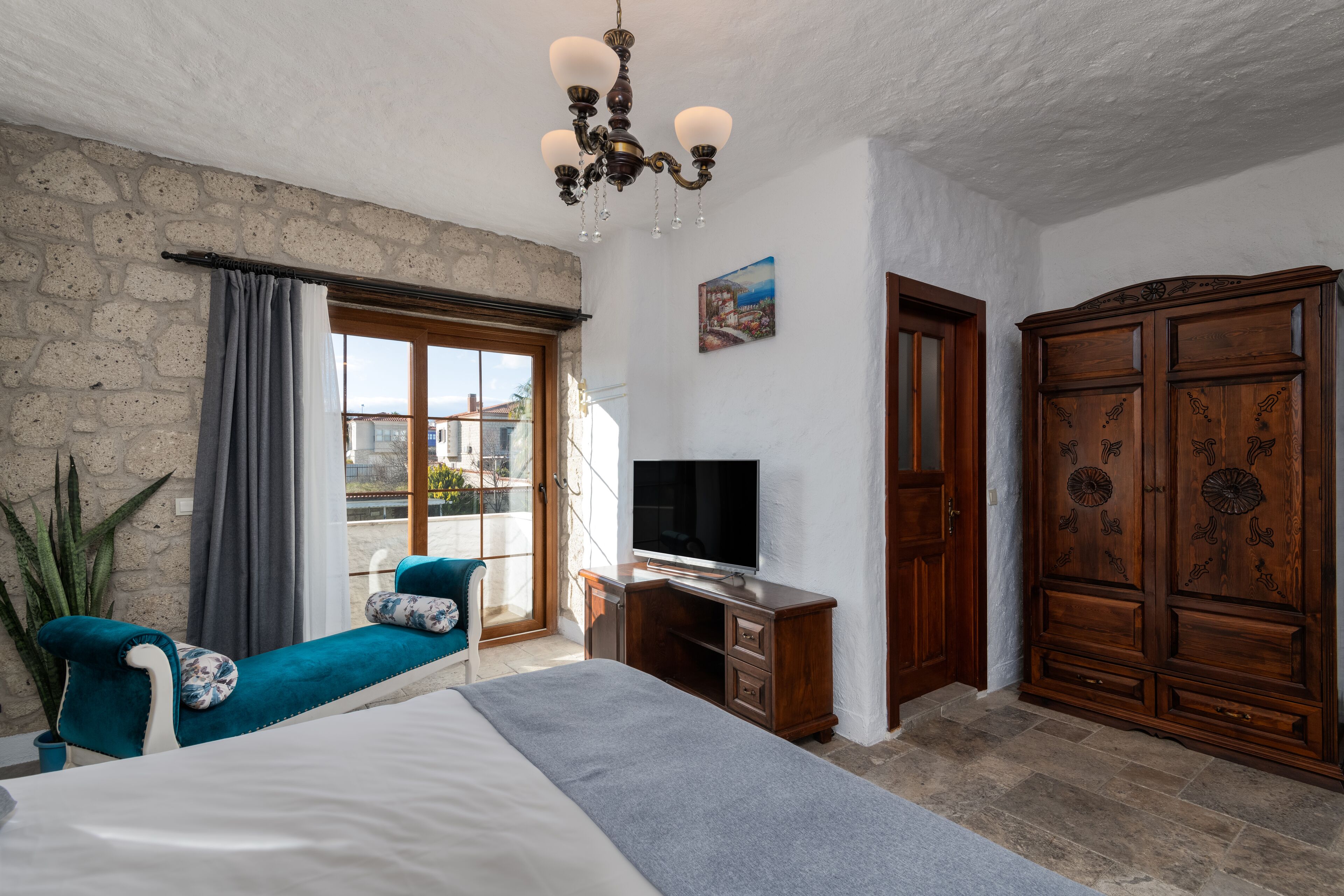 Un dormitorio con cama, televisión, armario de madera, escritorio y balcón con vistas.
