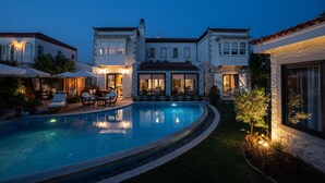 Una piscina con sillones de descanso y un patio bien iluminado.