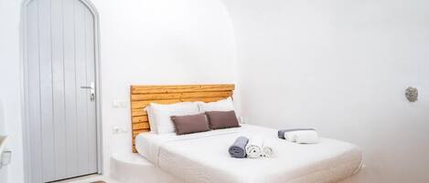 A bedroom with a wooden headboard, a white bedspread, and two rolled towels on the bed.
