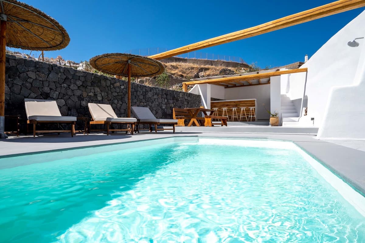 A pool area with lounge chairs and umbrellas, a stone wall, and a wooden deck.