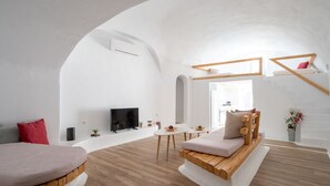 Uma sala de estar moderna e integrada, com teto curvo, piso de madeira, área de estar central com sofá e poltronas, uma mesa pequena e uma televisão.