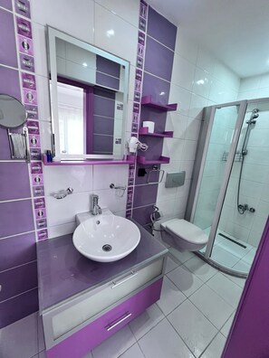 A bathroom with a sink, mirror, toilet, and glass shower enclosure. - Dardanos Pansiyon (Çanakkale)