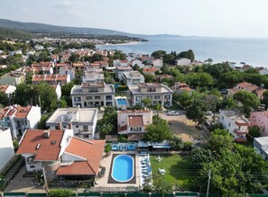 A coastal residential area with a swimming pool, multiple buildings, and a view of the sea. - Dardanos Pansiyon (Çanakkale)