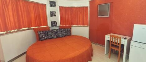 Un dormitorio con cama redonda, un escritorio y una silla.
