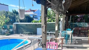 Zona de piscina al aire libre con mesa y sillas de vidrio, un ventilador colgante y un área de estar cubierta.