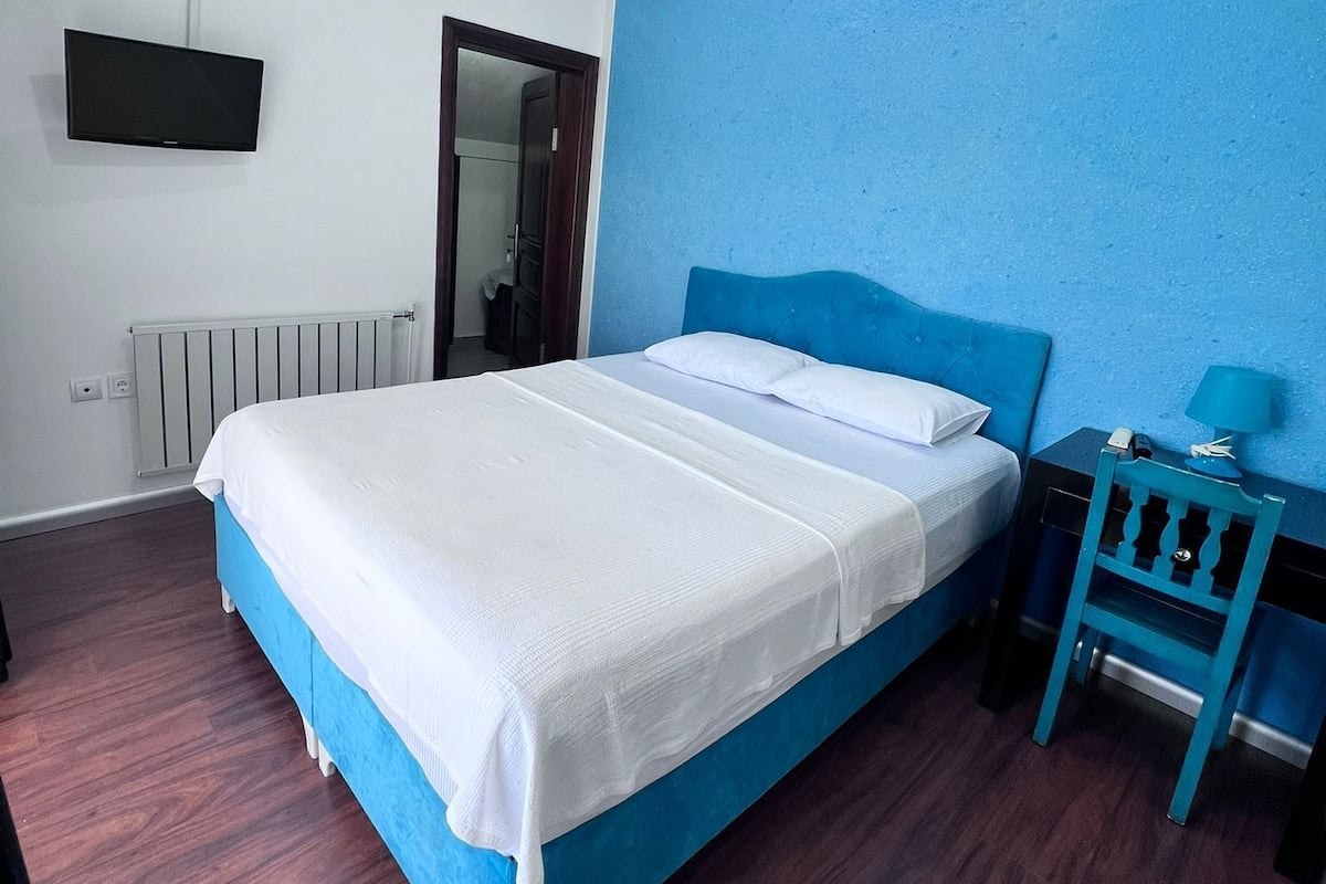 A bedroom with a bed, a TV, a nightstand, and a blue wall.