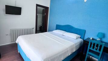 A bedroom with a bed, a TV, a nightstand, and a blue wall.