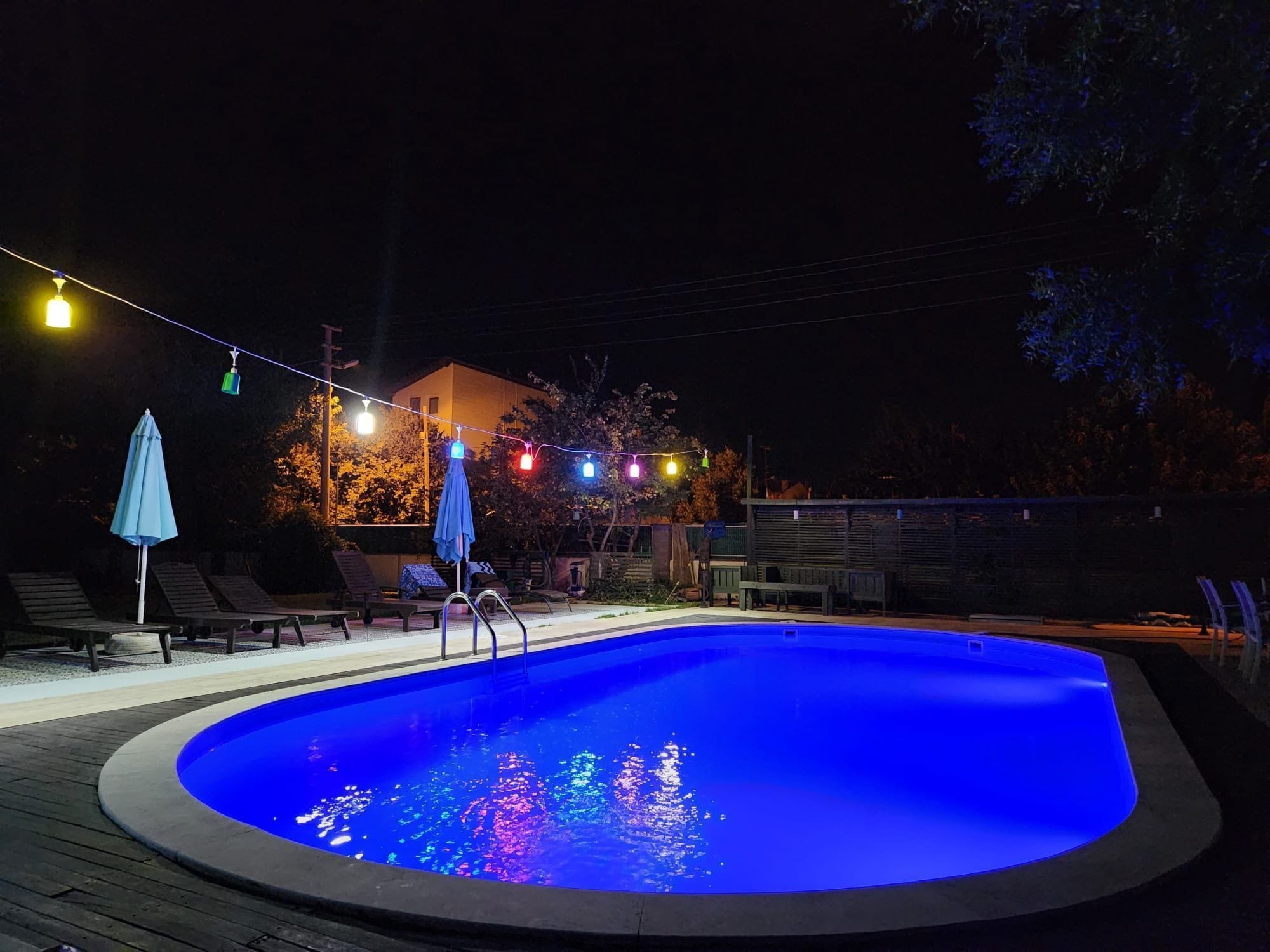 Una piscina de borde curvo, rodeada de sillas de descanso y una sombrilla azul.