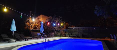 Una piscina de borde curvo, rodeada de sillas de descanso y una sombrilla azul.