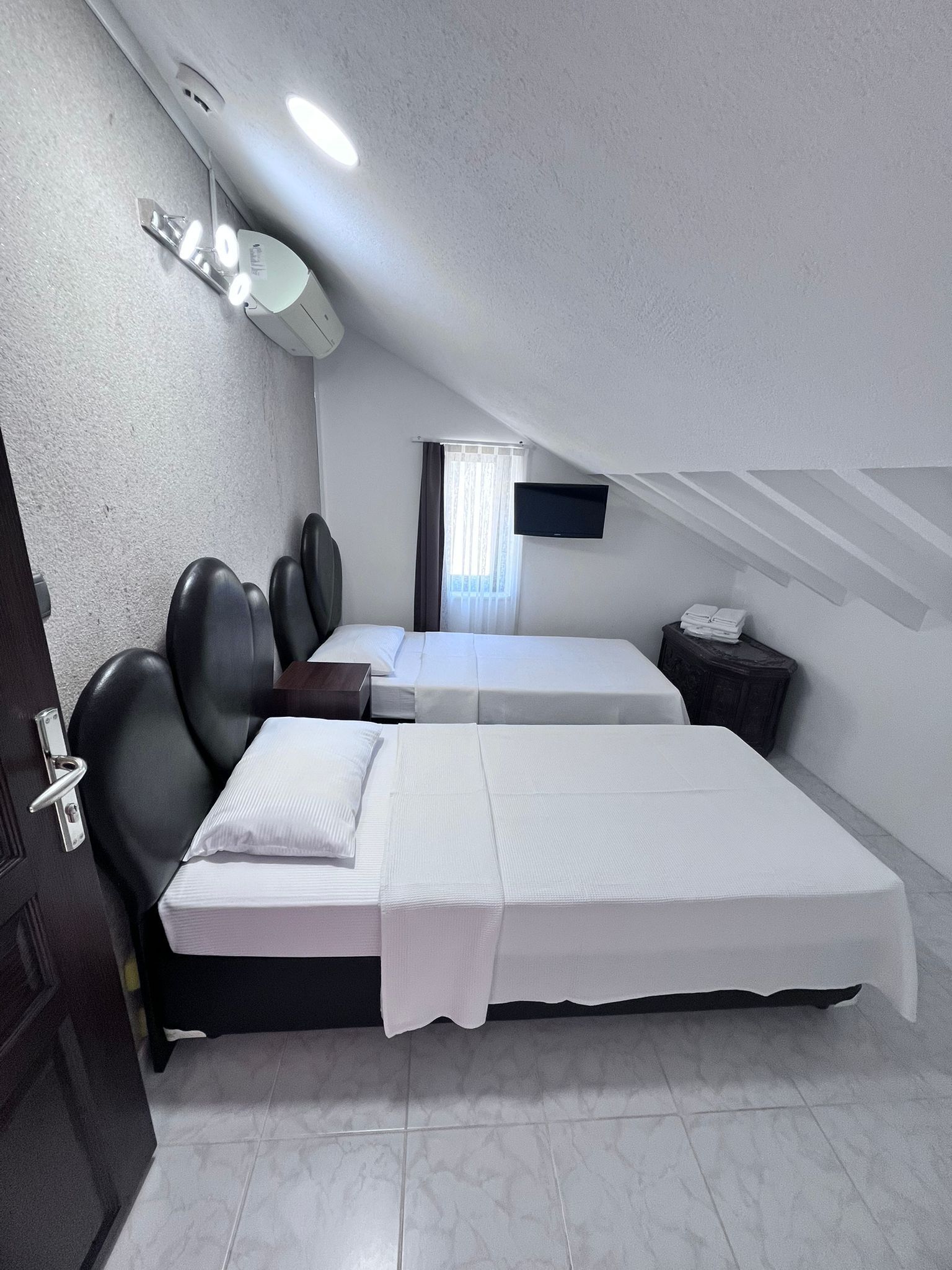 A room with two beds, a TV, a window with curtains, and a door.