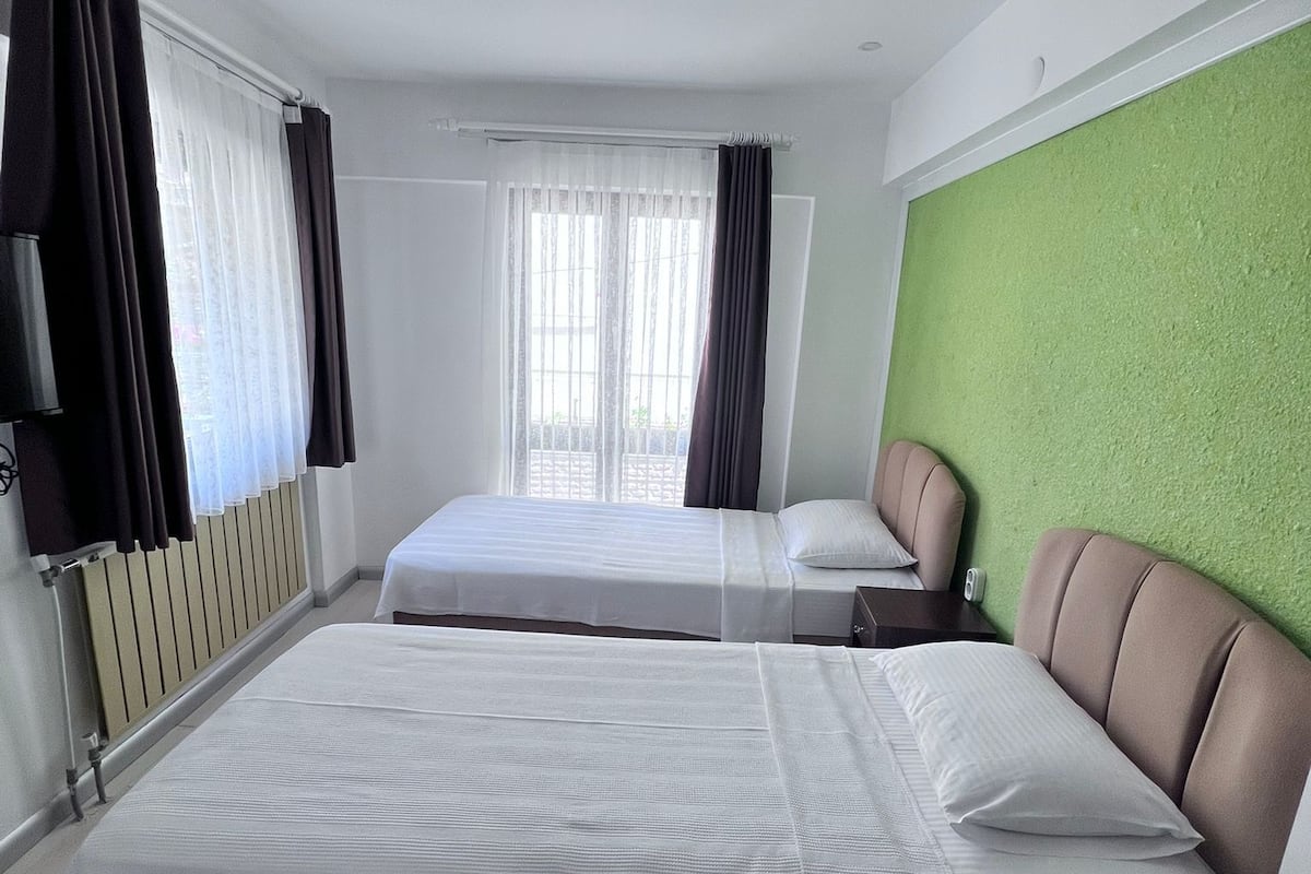 A hotel room with two beds, a green accent wall, and a window with curtains.