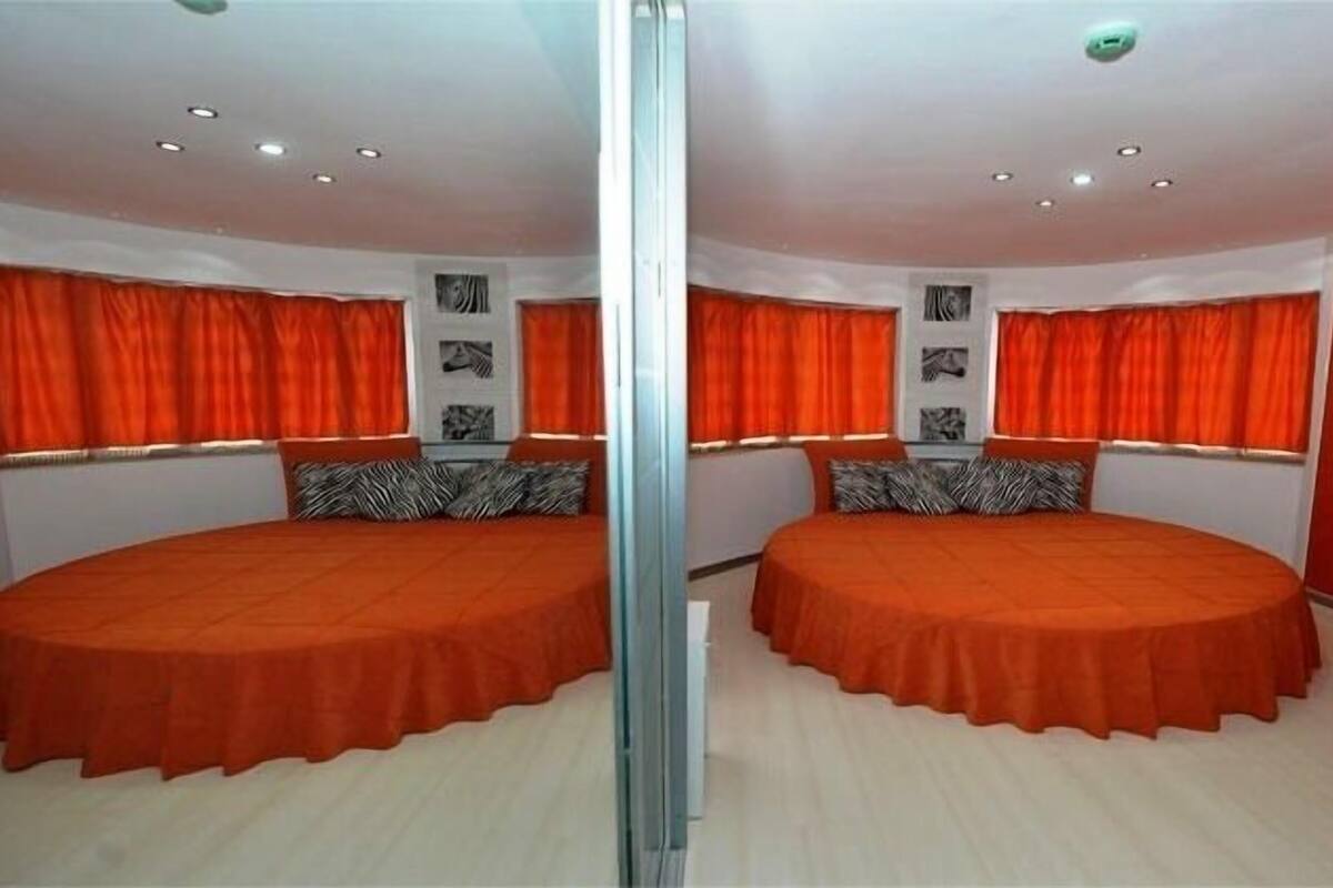 A mirrored room with two beds, red curtains, and a small table.