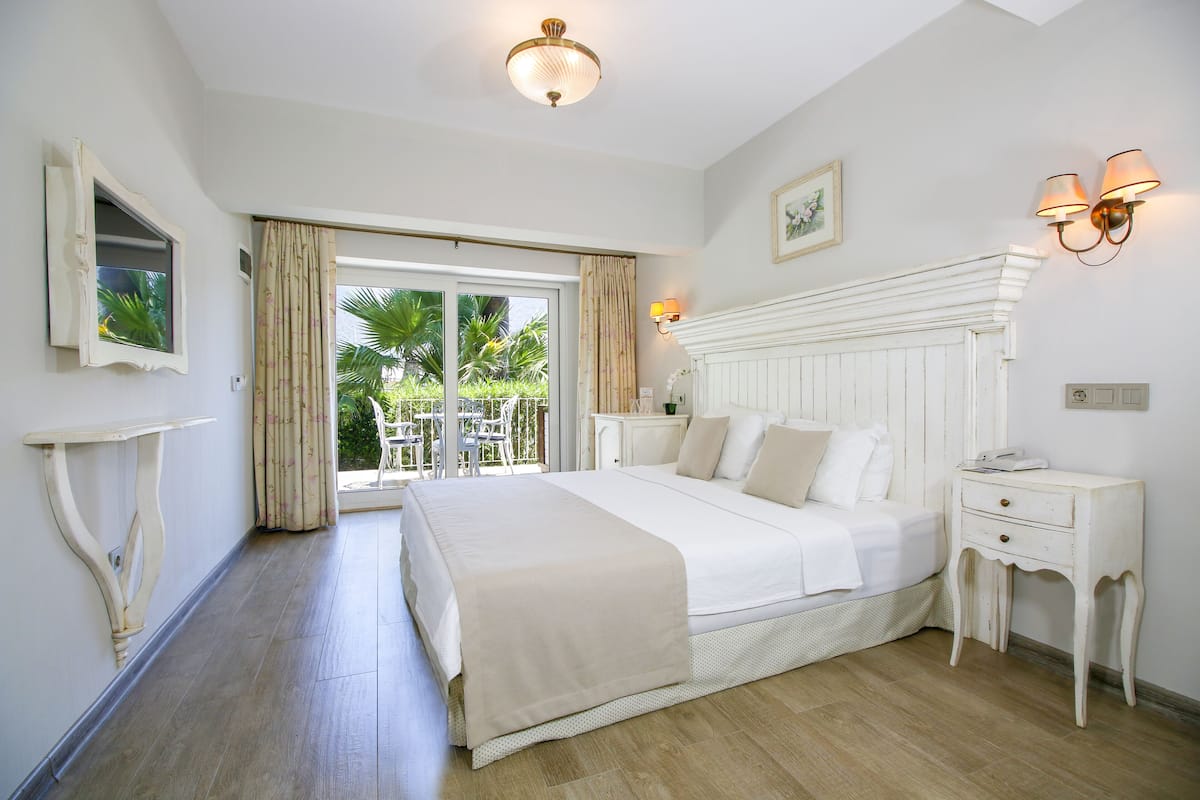 A spacious bedroom with a large bed, a bedside table, a nightstand, and a view of the outdoors.