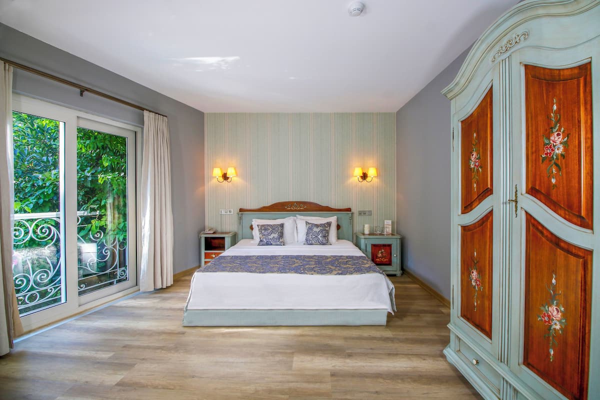 A bedroom with a large bed, a wooden wardrobe, and a balcony with a view of greenery.