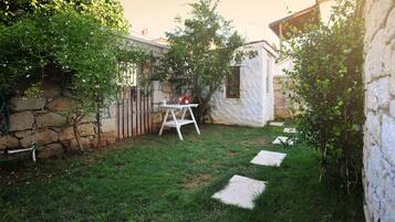 A small backyard with a stone wall, a wooden fence, a white table with flowers, and a paved path.