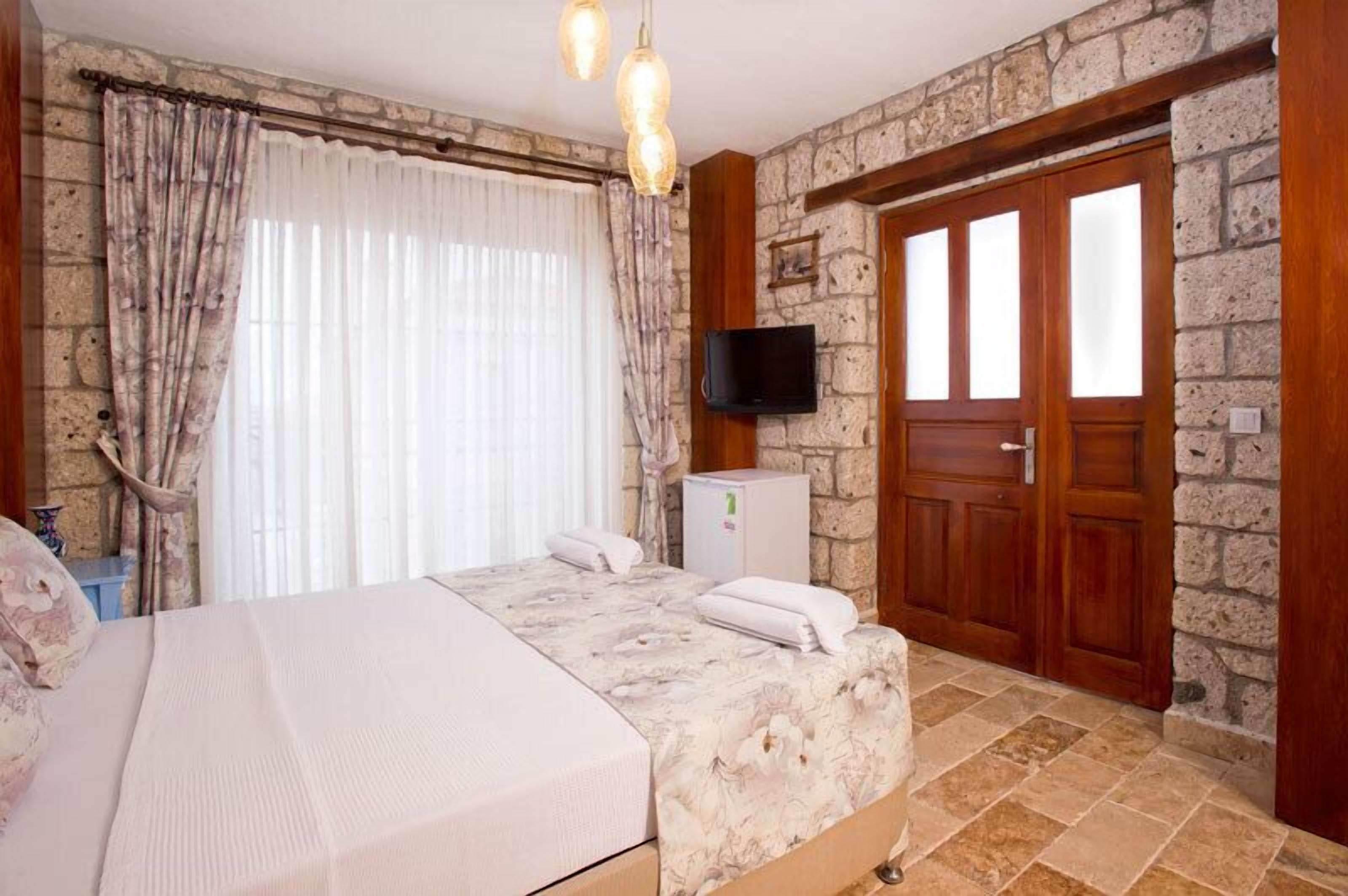 A bedroom with a bed, curtains, a television, and a stone wall.