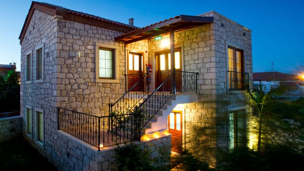 Una casa de pedra amb un balcó, una escala i l'interior il·luminat.