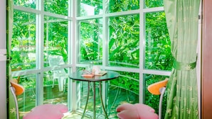 A room with a large glass window, a small round table, and two pink chairs. - Chalong Hill Tropical Garden Homes (Chalong)