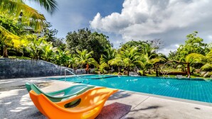 A swimming pool with a colorful boat-shaped lounge chair, surrounded by lush greenery and palm trees. - Chalong Hill Tropical Garden Homes (Chalong)