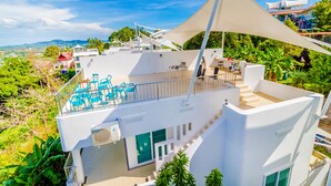 A modern white building with a rooftop terrace, outdoor seating, and a view of the surrounding landscape. - Chalong Hill Tropical Garden Homes (Chalong)