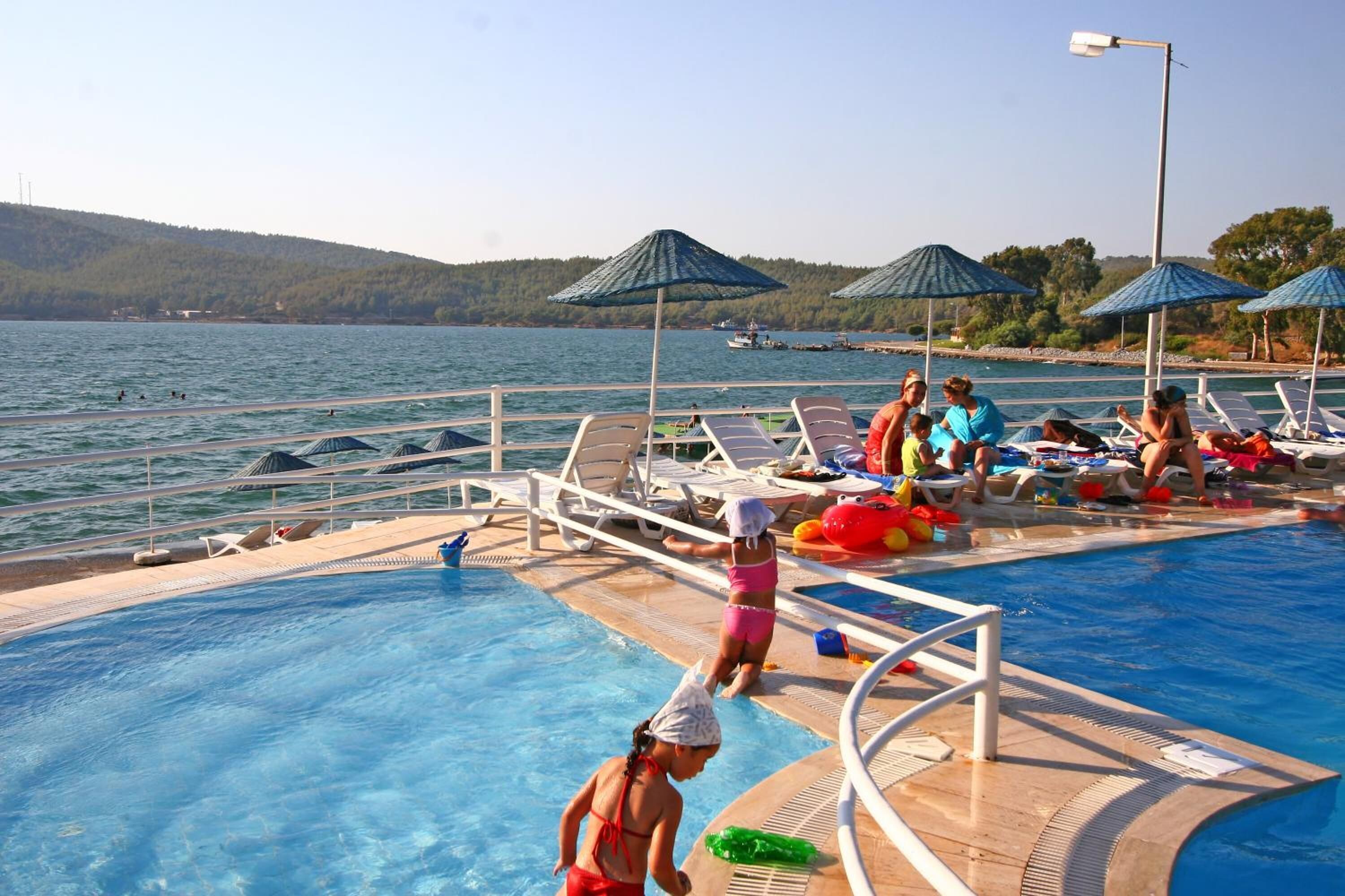 A swimming pool with lounge chairs and umbrellas, surrounded by water and hills.