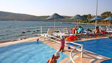 A swimming pool with lounge chairs and umbrellas, surrounded by water and hills.