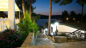 Una escalera de piedra que conduce a una zona de piscina con vistas al agua y árboles al atardecer.