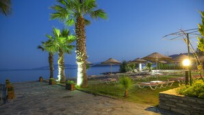 Een terras aan het strand met stenen vloer, palmbomen en strandparasols.