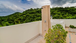 A rooftop with a shower, a white wall, and a view of a lush green hill. - Sea View Hua Hin Condos (Hua Hin)