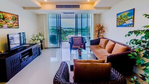 A modern living room with a flat-screen TV, a sofa, a coffee table, and a balcony with a view of the city. - Sea View Hua Hin Condos (Hua Hin)