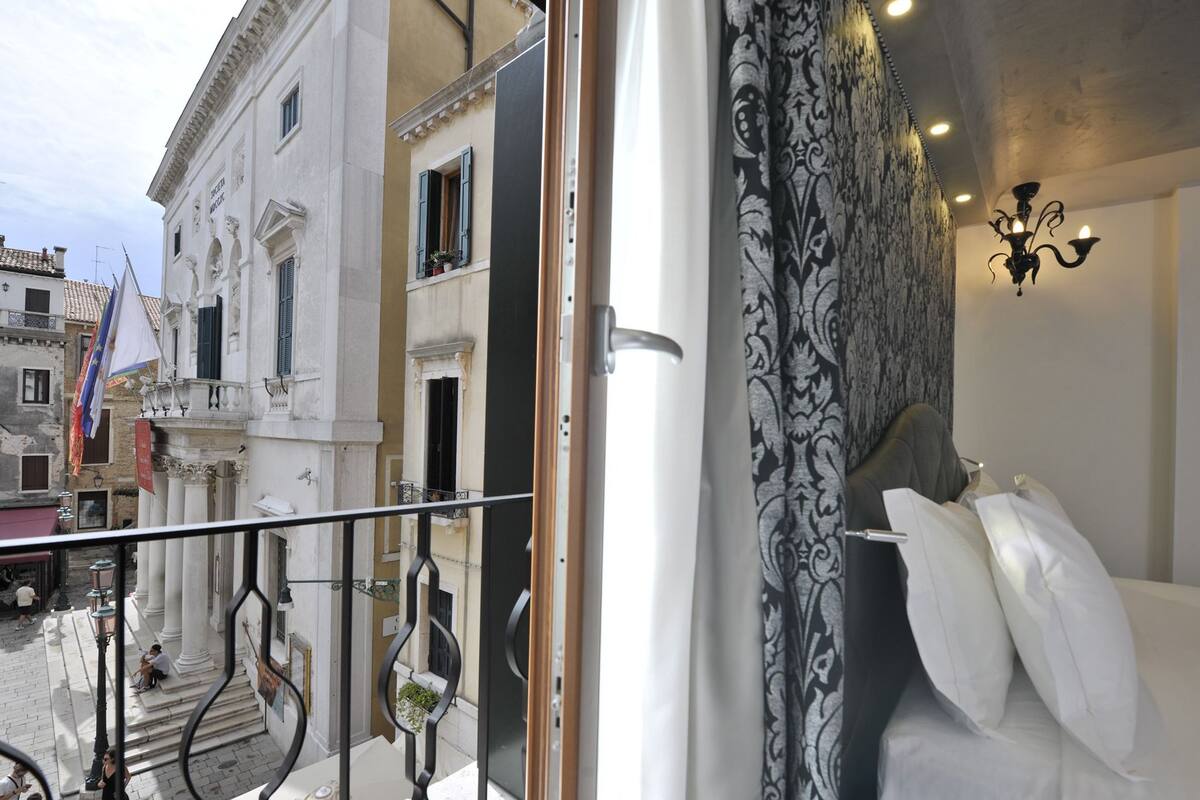 Habitación de hotel con balcón, candelabro y vista a la calle.