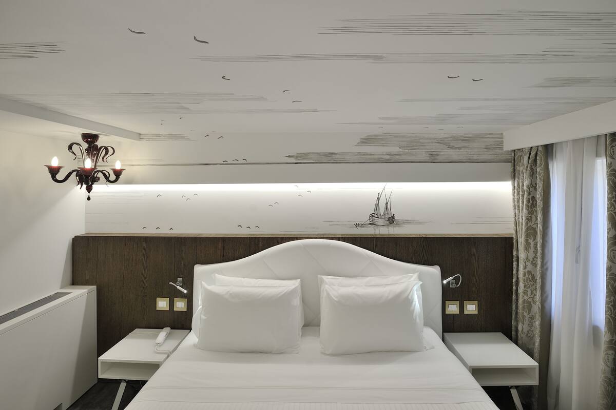 Una habitación de hotel moderna con una cama grande, mesitas de noche, un teléfono y un mural decorativo en el techo.