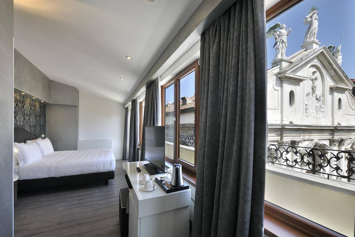 Habitación de hotel con una cama, un escritorio con ordenador y vistas a un edificio con estatuas.