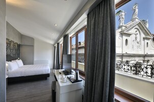 Una camera d'albergo con un letto, una scrivania con un computer e vista su un edificio con statue.