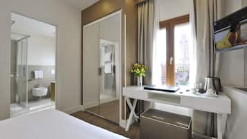 Quarto de hotel moderno com uma cama grande, uma escrivaninha com cafeteira, um espelho e vista para a cidade pela janela.