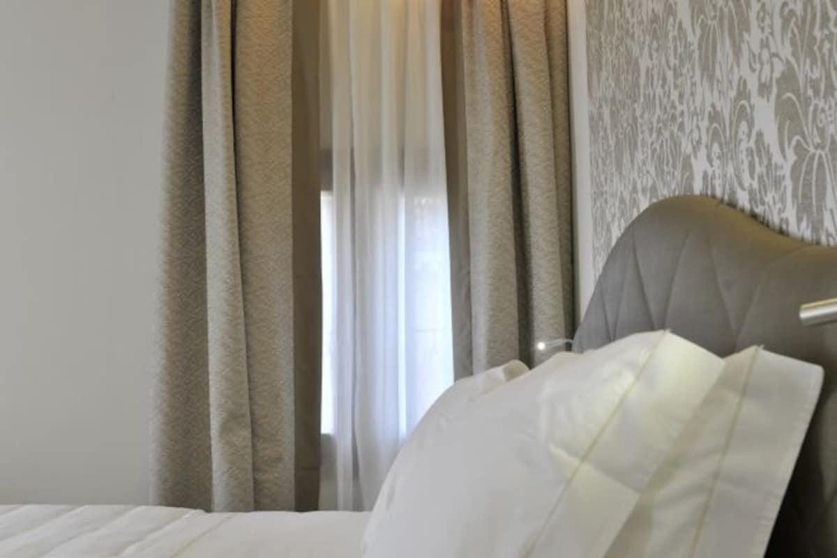 A hotel room with a bed, curtains, and a patterned wall.