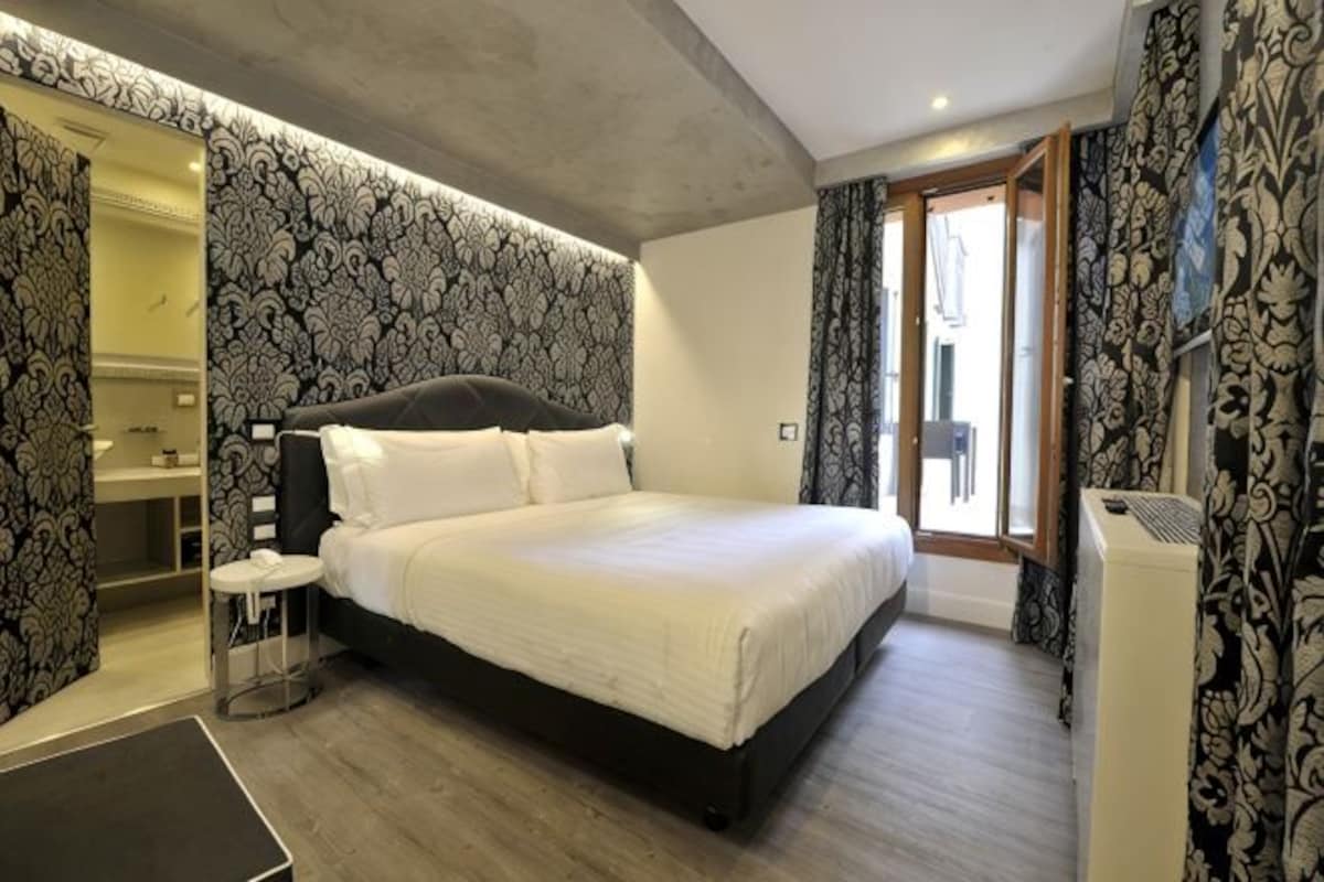A bedroom with a large bed, a bedside table, a mirror, and a wardrobe.