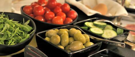 A buffet with various food items including tomatoes, cucumbers, olives, and greens.