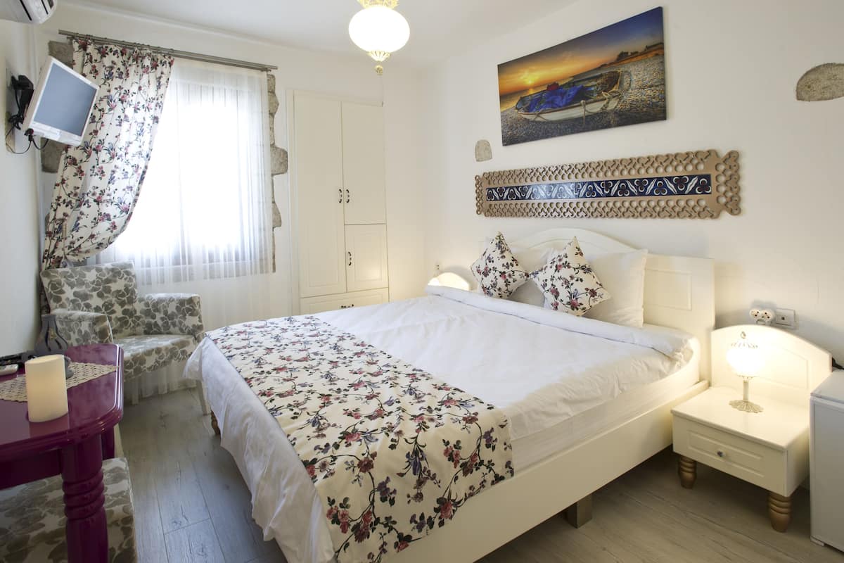 Un dormitorio con cama, mesita de noche, lámpara, televisor y ventana con cortinas.