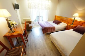A hotel room with two beds, a desk with a lamp, a chair, and a view of the outdoors through a window. - Le Griou (Saint-Jacques-des-Blats)