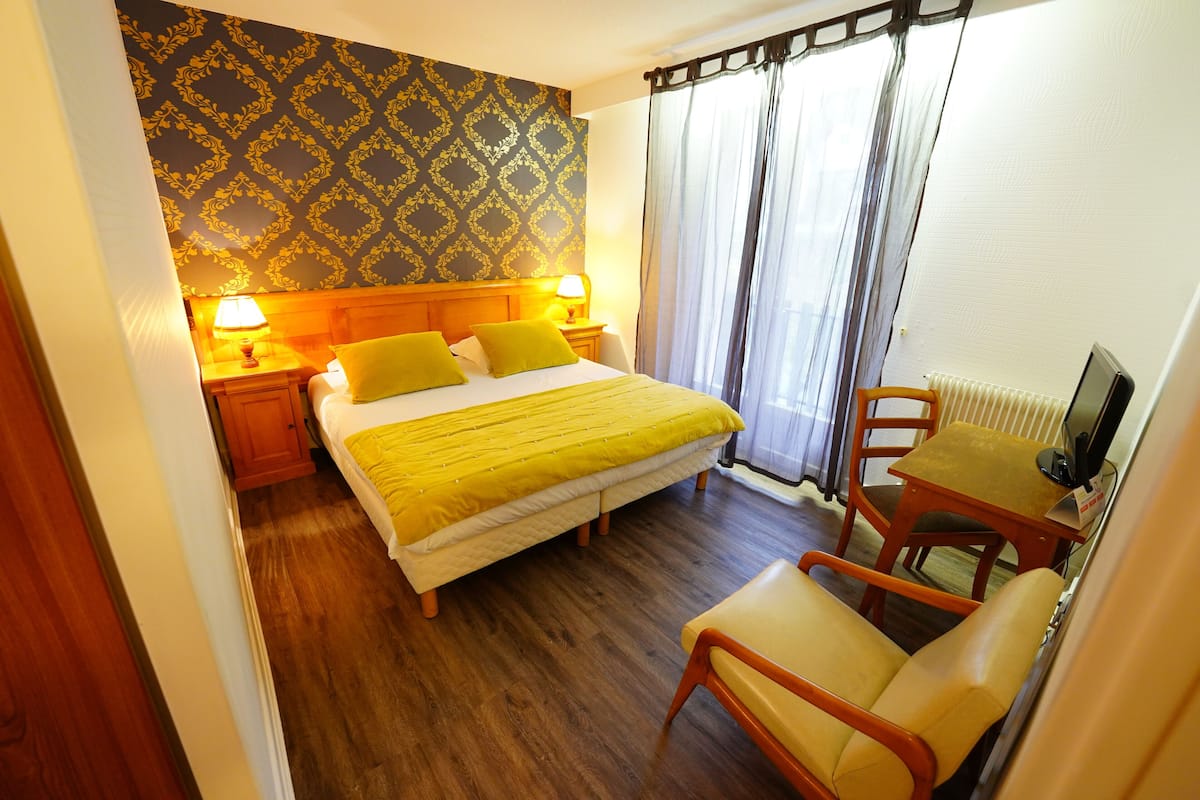 A hotel room with a bed, two bedside lamps, a chair, a small table, and a television.