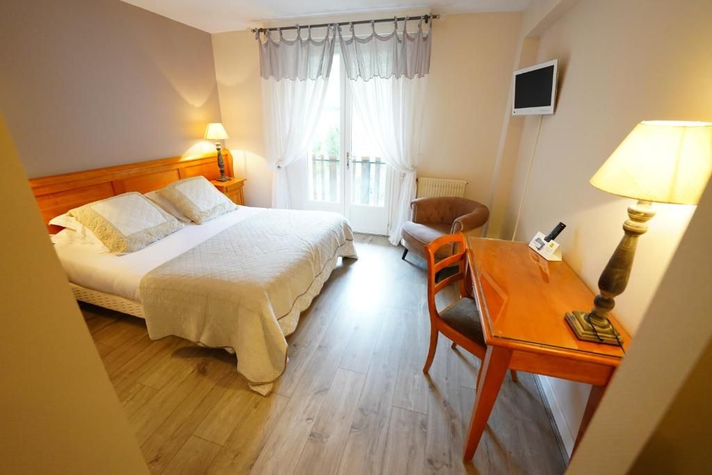 A hotel room with a bed, a desk, a chair, a television, and a window with curtains.