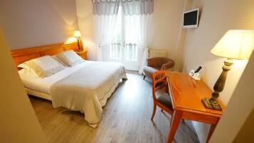 A hotel room with a bed, a desk, a chair, a television, and a window with curtains.