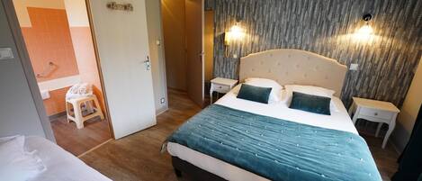 Hotellihuone, jossa on suuri sänky, kaksi yöpöytää, pieni sivupöytä, kylpyhuone, joka näkyy avoimesta ovesta, ja kuviollinen tapetti.