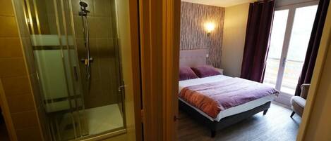 A hotel room with a shower, a bed with a headboard, and a window with curtains.