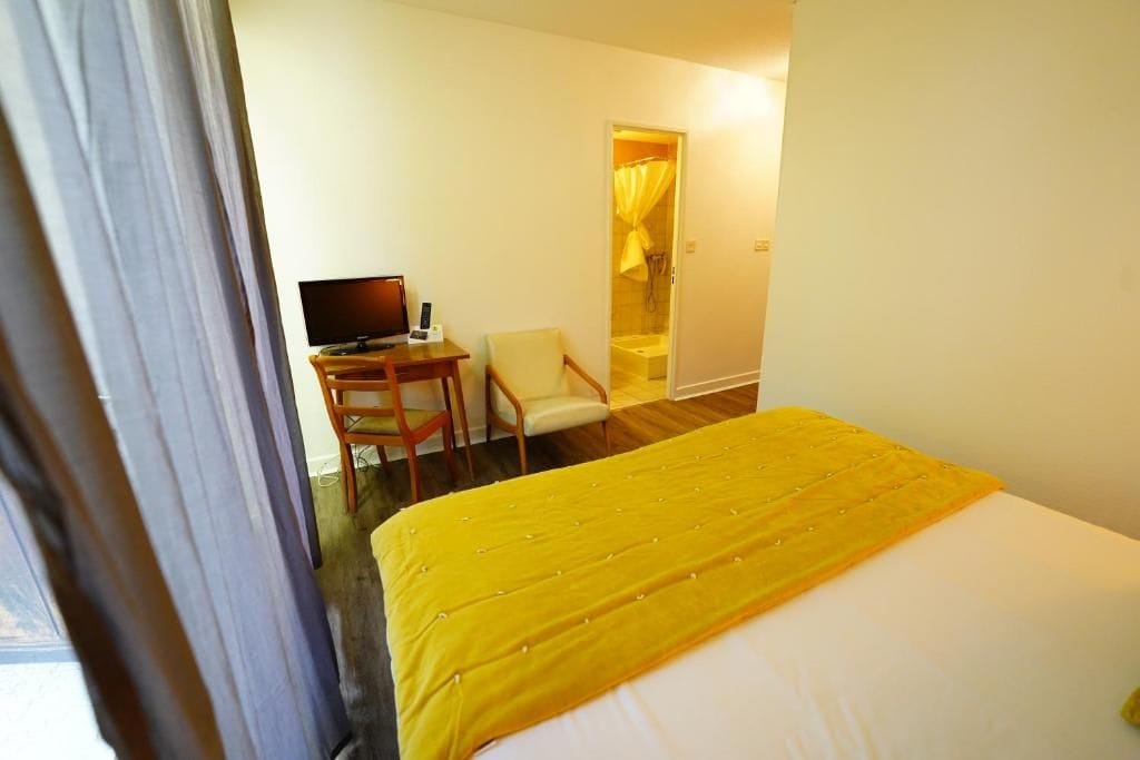 A hotel room with a bed, a desk with a computer, a chair, and a bathroom visible through an open door.