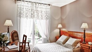 Una habitación de hotel con una cama, dos mesitas de noche con lámparas, una silla, un escritorio con lámpara y un ventanal con cortinas.