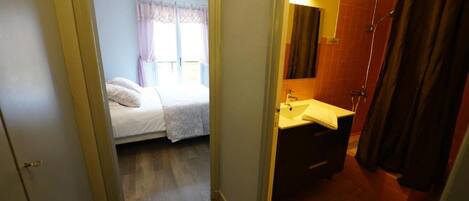 A bedroom with a bed, a bathroom with a sink and mirror, and a shower area.